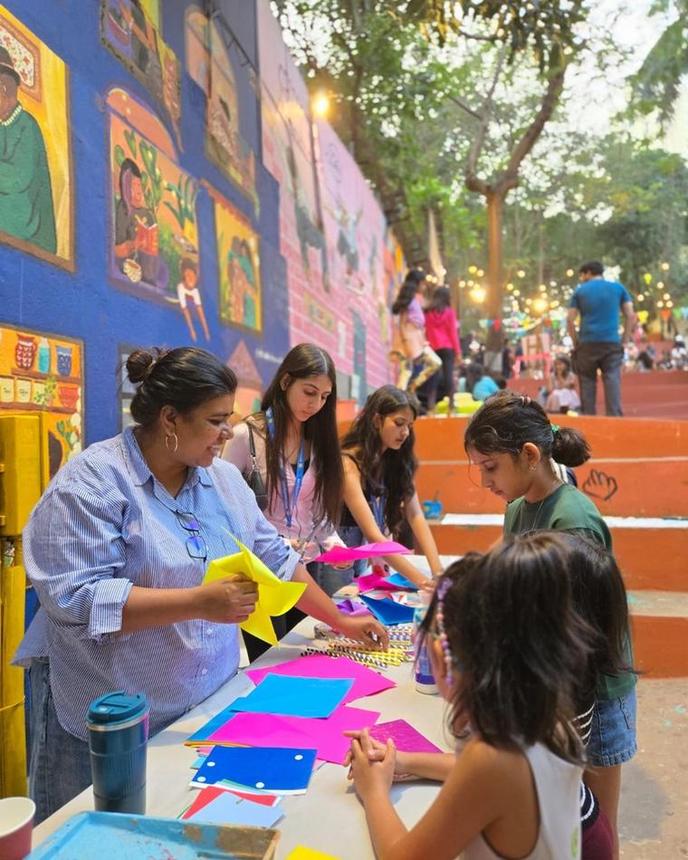 Children and adults painting together at a long table beside the murals
