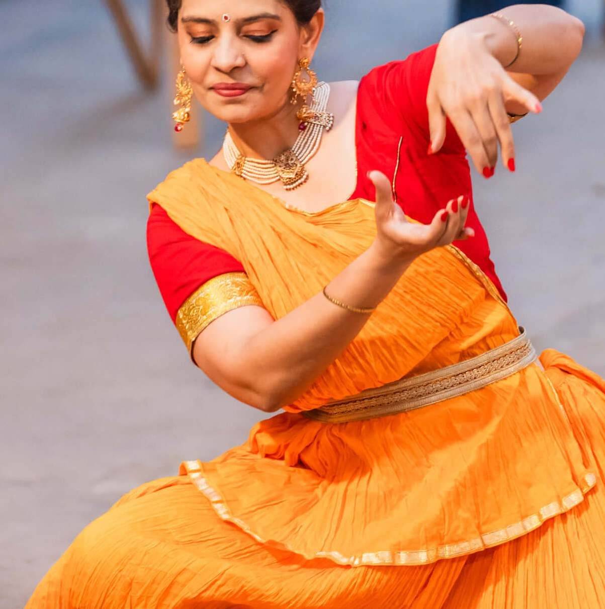 A Bharatanatyam dancer in an orange costume mid-performance