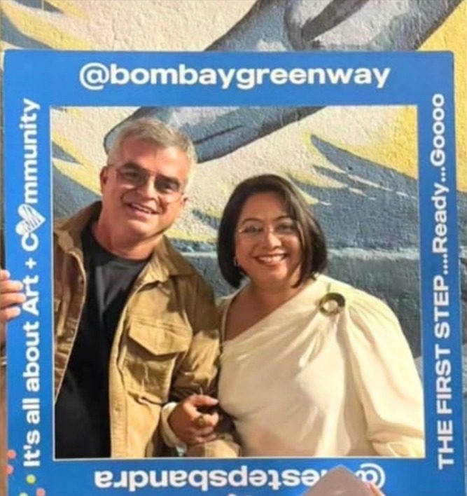 Atul Khatri and Faye D'Souza smiling through a blue Bombay Greenway photo frame at The Steps