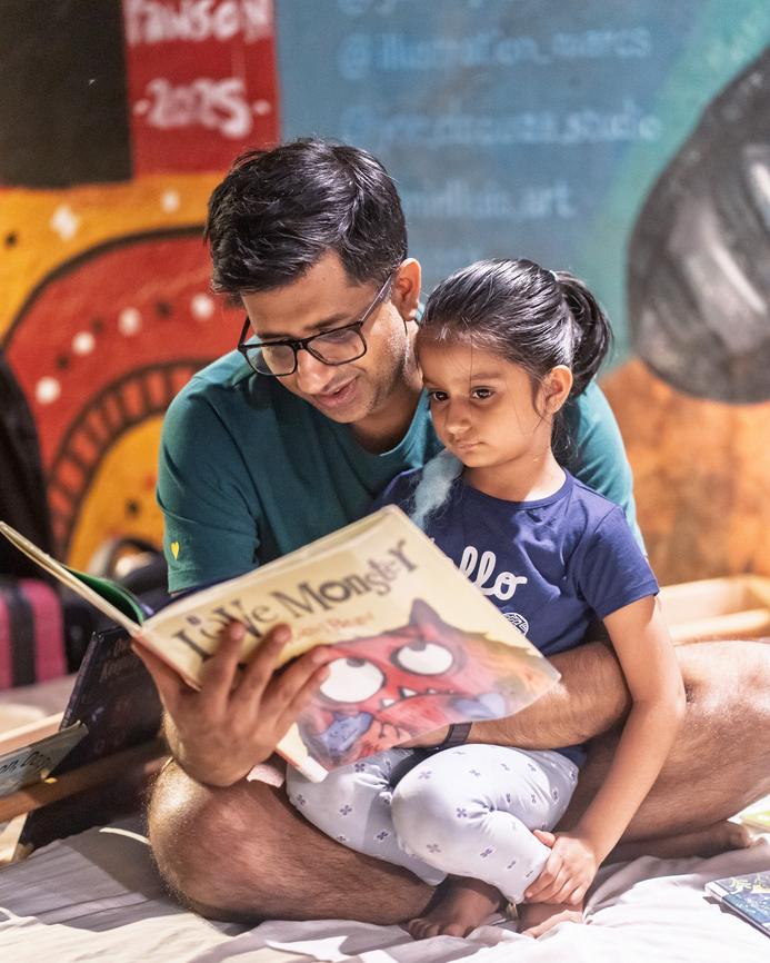 A father reading a book with his daughter in front of a painted wall