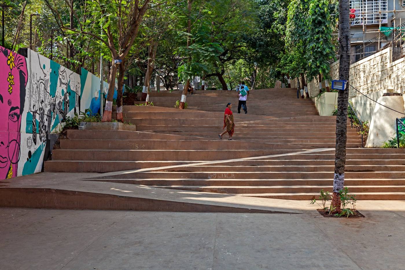 A woman walking up The Steps by day, past a large pink and teal mural